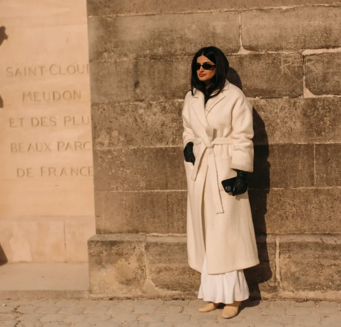 a woman wearing a long cream coat with leather gloves at Paris Fashion week FW23