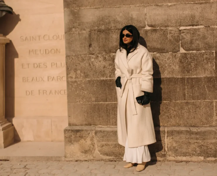 a woman wearing a long cream coat with leather gloves at Paris Fashion week FW23