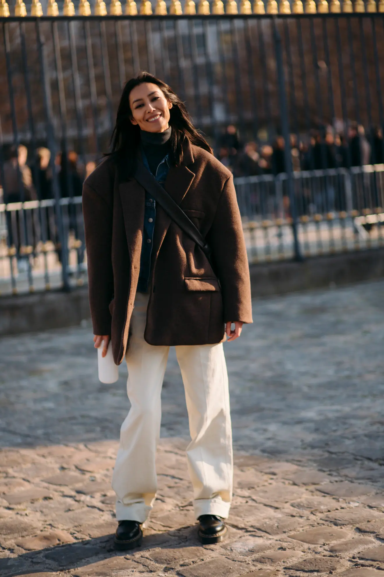 Parisian woman wearing a brown oversized blazer over a black turtleneck, white straight-leg pants 