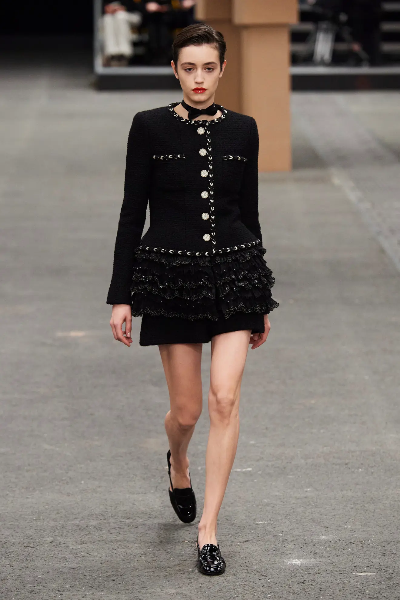 a woman wearing a Chanel little black dress with black patent leather loafers